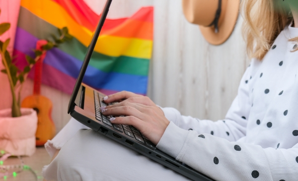 Persona en la computadora con una bandera LGBT al fondo