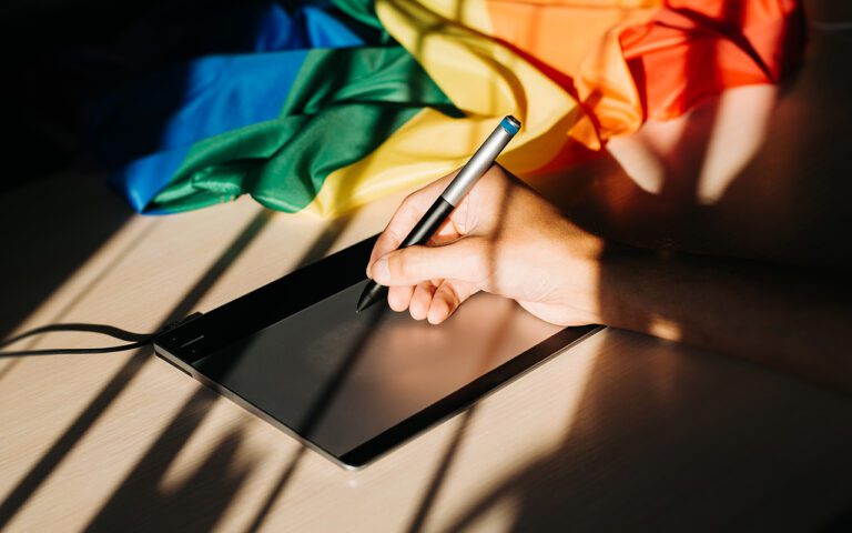Una persona escribiendo en una tableta con una bandea LGBT de fondo